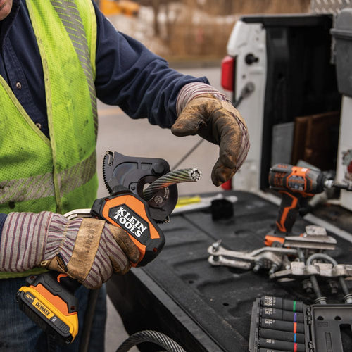 A person in a lime green safety vest cutting wires using a battery-operated wire cutter on the back of a truck.