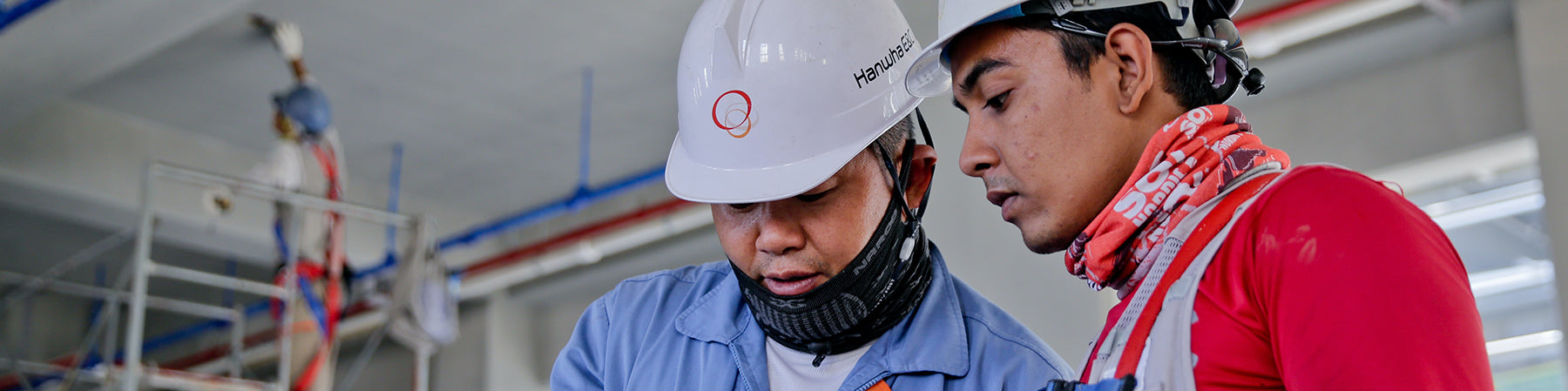 Two people wearing white hardhats look at paper at a construction site.