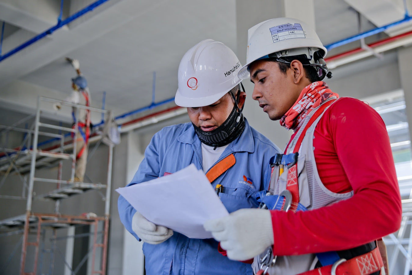 Two people wearing white hardhats look at paper at a construction site.